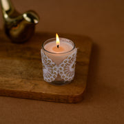 Decorative lace-wrapped candle in glass holder on wooden tray, warm brown background